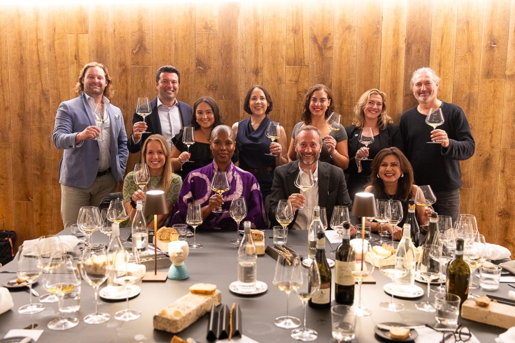 Un gruppo di giornalisti americani brinda durante una degustazione di vini Lugana, seduti attorno a un tavolo elegantemente apparecchiato.