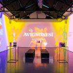 Installazione di un evento Avignonesi, con proiezioni colorate su pareti e bottiglie di vino in esposizione.